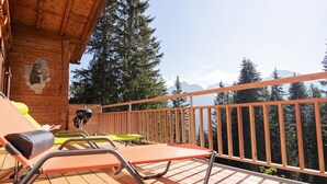 Une terrasse en bois avec des chaises longues et un barbecue, offrant une vue sur une zone montagneuse boisée.