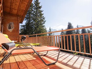 A wooden deck with lounge chairs and a barbecue grill, overlooking a forested mountain area. - Chalet Soldanella by Arosa Holiday Appartement/Fewo, Dusche oder Bad, WC, 9-Bett by Interhome (Arosa)