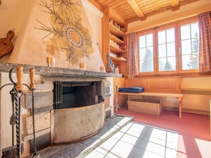 A cozy room with a stone fireplace, wooden shelves, and a large window with curtains. - Chalet Soldanella by Arosa Holiday Appartement/Fewo, Dusche oder Bad, WC, 9-Bett by Interhome (Arosa)
