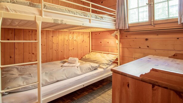 Une chambre avec un lit superposé, un intérieur en bois, une fenêtre avec des rideaux et une petite table.
