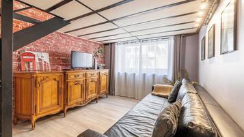 A living room with a sofa, wooden cabinet, television, and a brick wall.