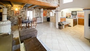 Un interior rústic amb parets de pedra, zona de menjador, cuina i una llar de foc.