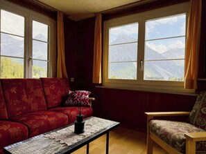 A cozy room with a red sofa, a small table with a vase, and a chair. Large windows offer a view of mountains. - Chalet Methfessel 3 by Arosa Holiday Appartement/Fewo, Bad, WC, 3 Schlafräume by Interhome (Arosa)