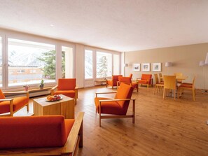 A spacious room with large windows, orange chairs, wooden tables, and a view of buildings outside. - Utoring Hohe Promenade 004 Appartement/Fewo, Dusche, WC, 2-Bettwohnung by Interhome (Arosa)