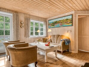 A room with wooden paneling, a painting of a coastal town, a table with a vase and candles, and a sofa. - "Alivia" - 500m from the sea by Interhome (Læsø)