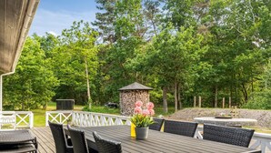Une terrasse extérieure avec une table et des chaises, entourée d’arbres et d’une structure en pierre.