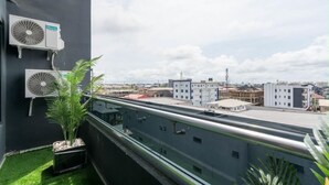 Een terras op het dak met twee airconditioners, een bloempot en een uitzicht op omliggende gebouwen.