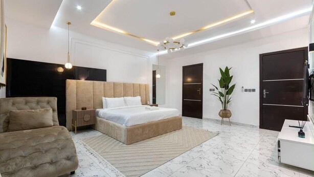 Een moderne slaapkamer met een groot bed, een bank, een nachtkastje en een potplant.