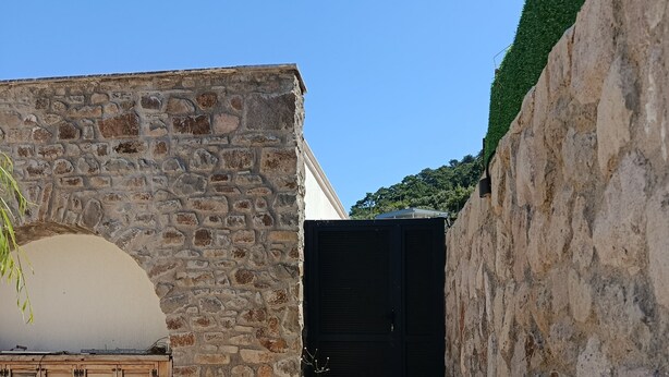 A stone wall with a wooden bench, a closed gate, and a paved pathway. - Therapy Igloo (Bodrum)