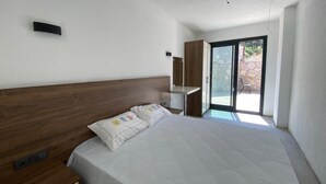 A bedroom with a wooden headboard, a bed with white bedding, a nightstand, a built-in wardrobe, and a sliding glass door leading to an outdoor area. - Therapy Igloo (Bodrum)