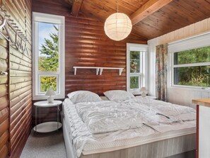 A bedroom with a wooden ceiling, a bed with white bedding, two bedside tables, and a hanging light fixture.
