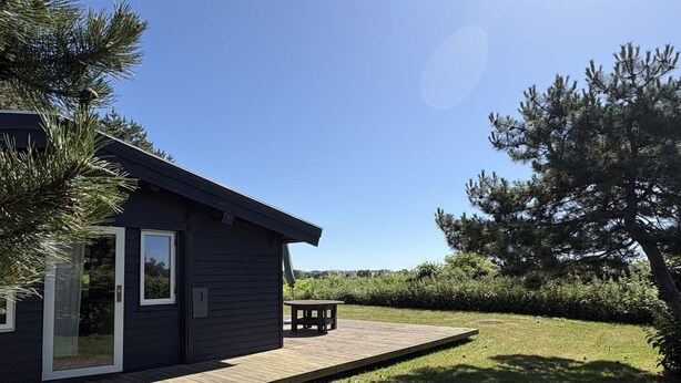 A dark-colored building with a deck, a table, and a large tree in the background. - "Vilmar" - 450m from the sea by Interhome (Nykøbing Sj)