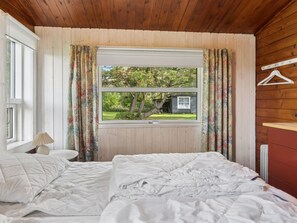 A bedroom with two beds, a window with curtains, a radiator, and a wooden ceiling.