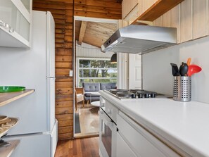 A compact kitchen with a stove, a range hood, and a window overlooking a garden.