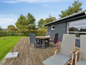 A deck with a table and chairs, a small house with a window, and a grassy yard with trees.
