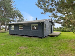 A small, single-story cabin with a front porch, surrounded by grass and trees.