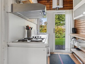 A compact kitchen with a gas stove, a stainless steel range hood, and a window overlooking a garden.