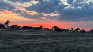 A beach with a sunset sky, sandy ground, and scattered buildings.