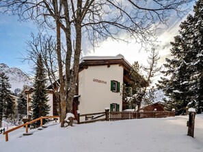 Ein mit Schnee bedecktes Gebäude mit Holzzaun, umgeben von Bäumen und Bergen.