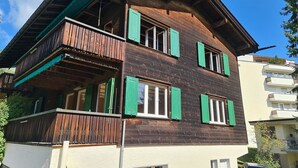 Een houten huis met twee verdiepingen, een balkon en meerdere ramen.
