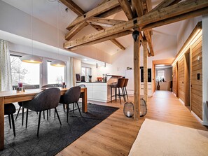 Eine moderne Küche mit Holzbalken, ein Essbereich mit Tisch und Stühlen sowie ein Flur, der zum Schlafzimmer führt.
