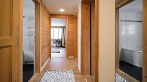 Een gang met houten wanden, een kamerbreed tapijt en zicht op een kamer met een stoel en gordijnen.