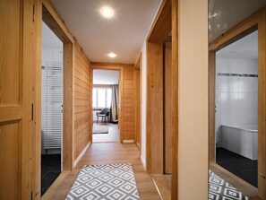 A hallway with wooden walls, a patterned rug, and a view into a room with a chair and curtains. - Grabahus Appartement/Fewo, Dusche oder Bad, WC, 9-Bettwohnung by Interhome (Arosa)