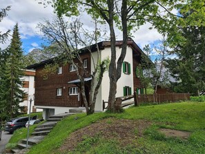 A two-story building with a brick facade and green shutters, surrounded by trees and a grassy area. - Grabahus Appartement/Fewo, Dusche oder Bad, WC, 9-Bettwohnung by Interhome (Arosa)