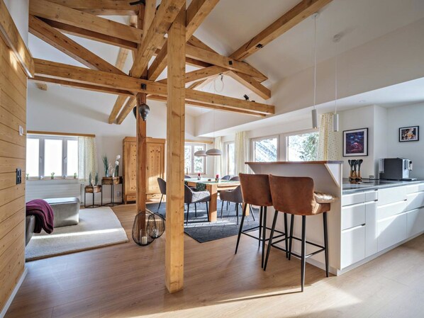 A spacious kitchen with wooden beams, a dining area with a table and chairs, and a bar area with stools. - Grabahus Appartement/Fewo, Dusche oder Bad, WC, 9-Bettwohnung by Interhome (Arosa)