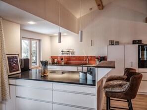 A modern kitchen with a central island, white cabinetry, and a bar area with two stools. - Grabahus Appartement/Fewo, Dusche oder Bad, WC, 9-Bettwohnung by Interhome (Arosa)