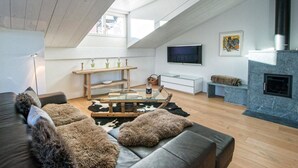A modern living room with a sloped ceiling, a fireplace, a television, and a sofa with fur throw pillows. - Juggasunna Appartement/Fewo, Dusche und Bad, WC, 7-Bettwohnung by Interhome (Arosa)