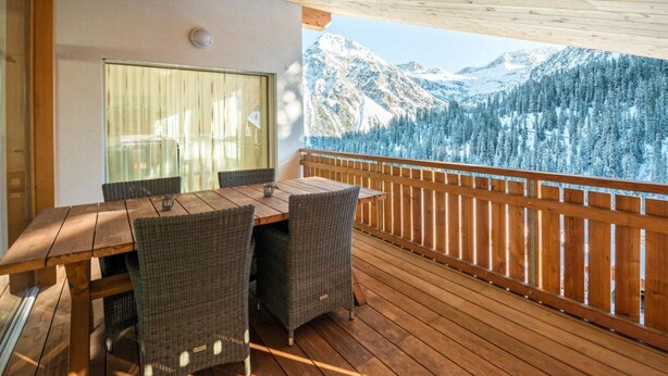 A wooden deck with a table and chairs, a glass wall, and a mountain view. - Juggasunna Appartement/Fewo, Dusche und Bad, WC, 7-Bettwohnung by Interhome (Arosa)