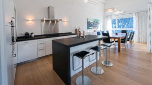 A modern kitchen with a central island, bar stools, a dining area with a table and chairs, and a large window with a view. - Juggasunna Appartement/Fewo, Dusche und Bad, WC, 7-Bettwohnung by Interhome (Arosa)
