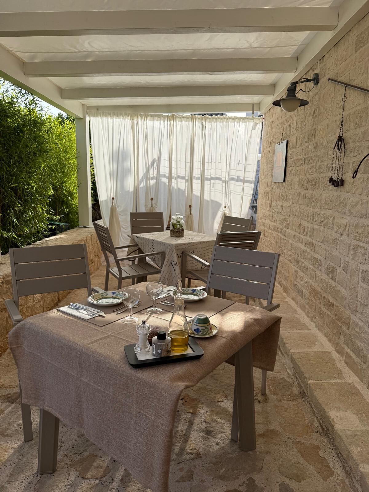 An outdoor dining area with a table set for two, surrounded by chairs, and a stone wall in the background.