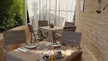 An outdoor dining area with a table set for two, surrounded by chairs, and a stone wall in the background.