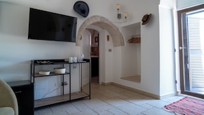 Una sala de estar con un televisor de pantalla plana, un mueble negro para equipo audiovisual, un arco de piedra y una puerta que da a otra habitación.