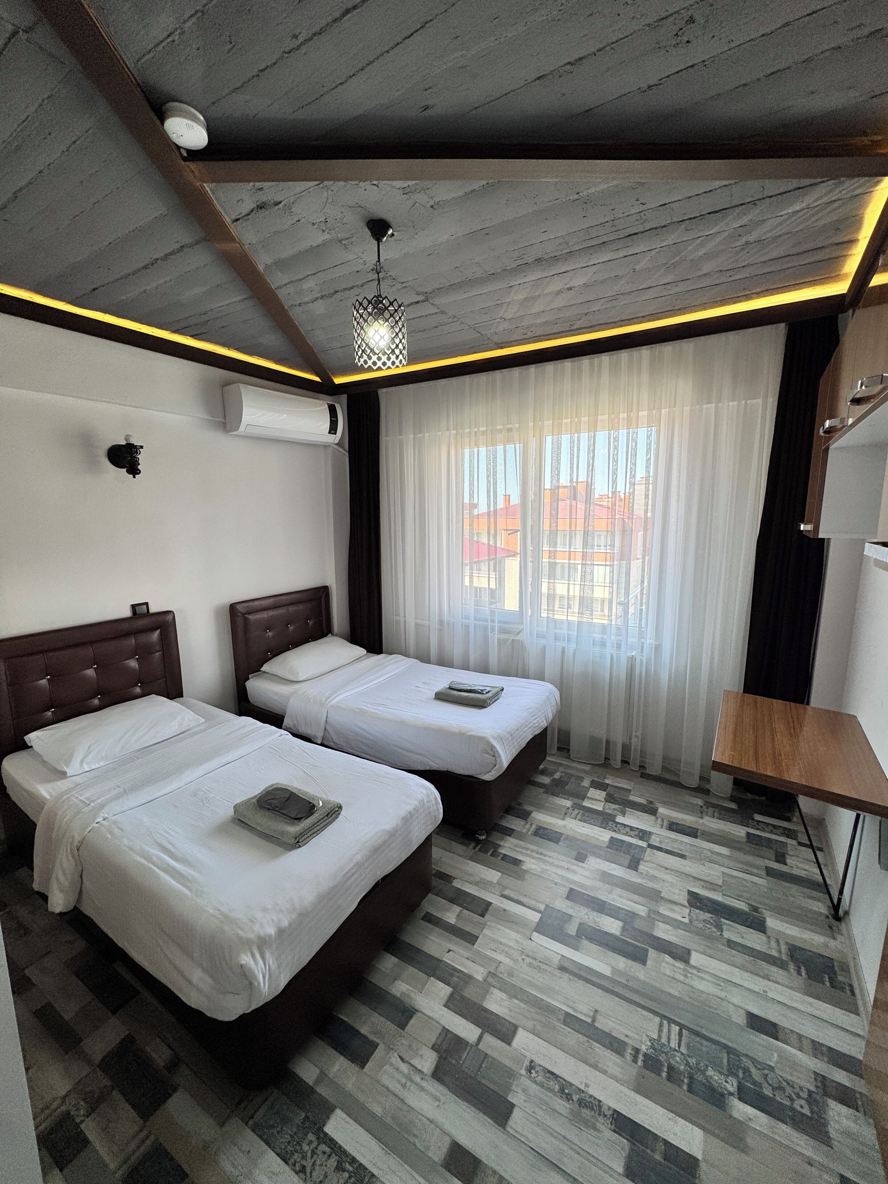 Habitación de hotel con dos camas, un escritorio pequeño, una ventana con cortinas y un suelo estampado.