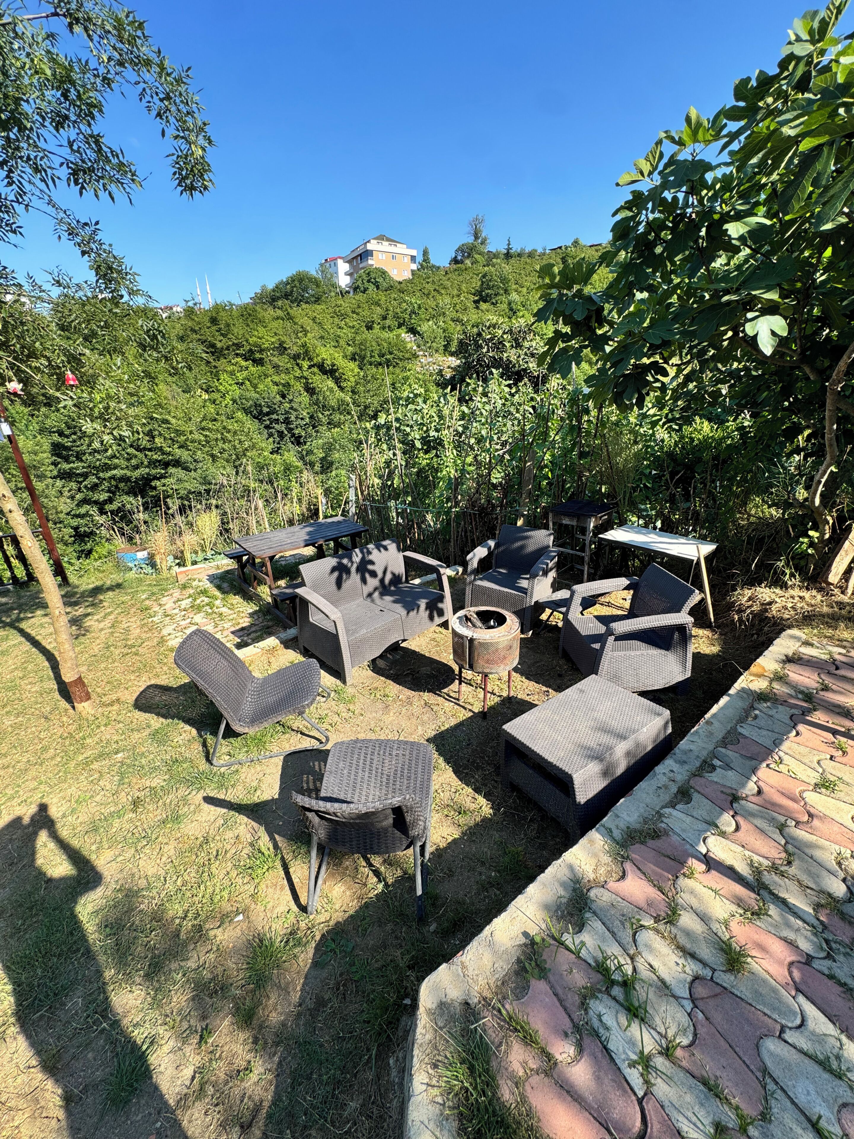 Un área de estar al aire libre con mobiliario de mimbre, un brasero y vistas a una colina con edificios.