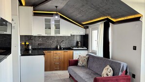 Cocina compacta con comedor, sofá y un banco rojo.