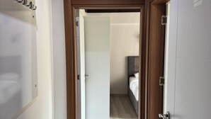 Un pasillo que conduce a un dormitorio con cama, un marco de puerta de madera y una pared blanca con un cartel.