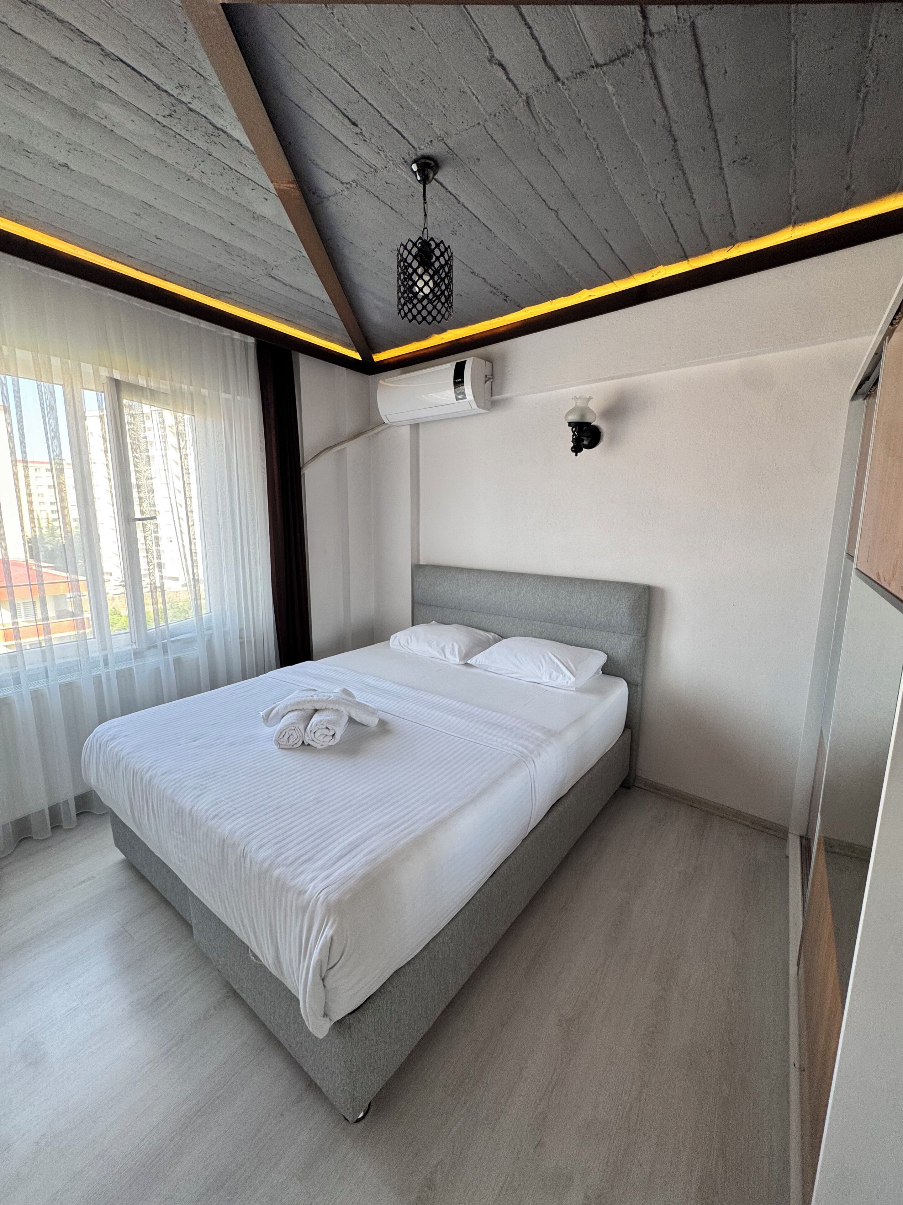 A modern bedroom with a bed, curtains, a ceiling light, and an air conditioning unit.