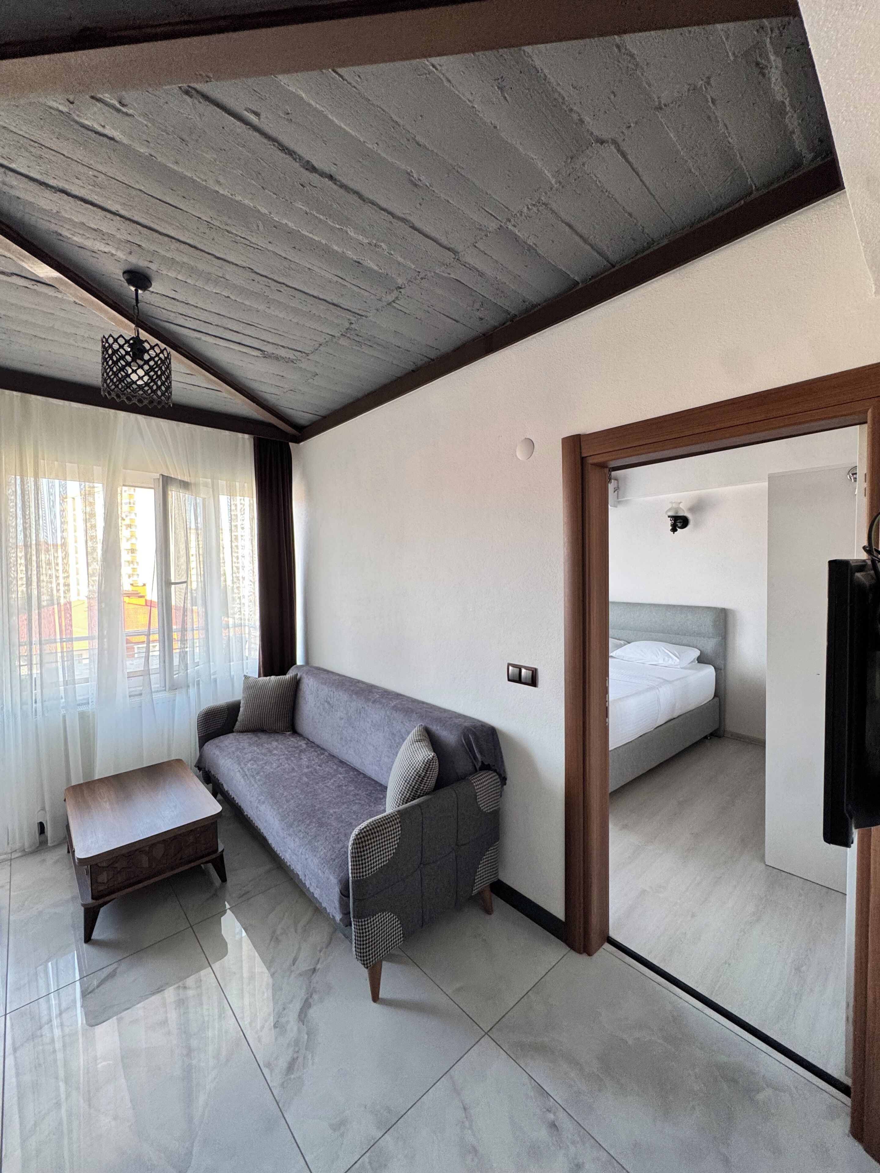 Una habitación moderna con un sofá gris, una pequeña mesa de madera, una cama y un espejo.