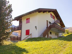 Eine zweistöckige Chalet mit Balkon, einer Holztreppe und einem Berg im Hintergrund.