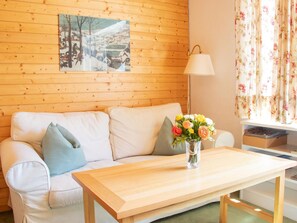 A wooden-paneled room with a white sofa, a wooden coffee table, a lamp, and a floral curtain. - Haus Christina Dohlengiebel Appartement/Fewo, Dusche und Bad, WC, 3 Schlafräume by Interhome (Arosa)