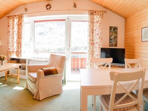 Ein gemütliches Zimmer mit Holzboden, einer Couch, einem Tisch, einem Fernseher und einem Balkon mit Bergblick.