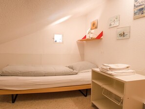 A small, single-bed room with a wooden frame, a bedside table with a lamp, and a wall-mounted shelf with pictures. - Haus Christina Dohlengiebel Appartement/Fewo, Dusche und Bad, WC, 3 Schlafräume by Interhome (Arosa)