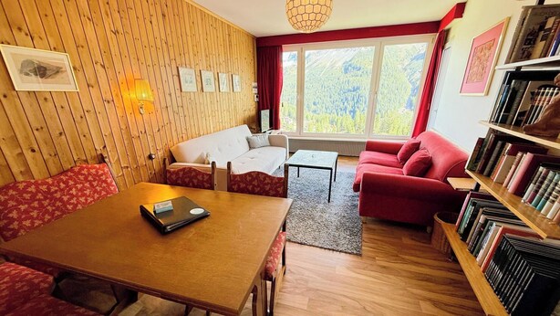 Una sala de estar acogedora con una pared de madera, un sofá rojo, un sillón rojo, una mesa de centro de madera y una estantería.