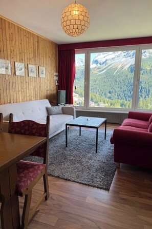Ein Zimmer mit einer Couch, einem Esszimmer und Blick auf Berge durch große Fenster.
