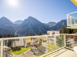 Blick auf Berge vom Balkon mit Glasgeländer, mit Blick auf ein Wohngebiet mit Häusern und blauem Himmel.