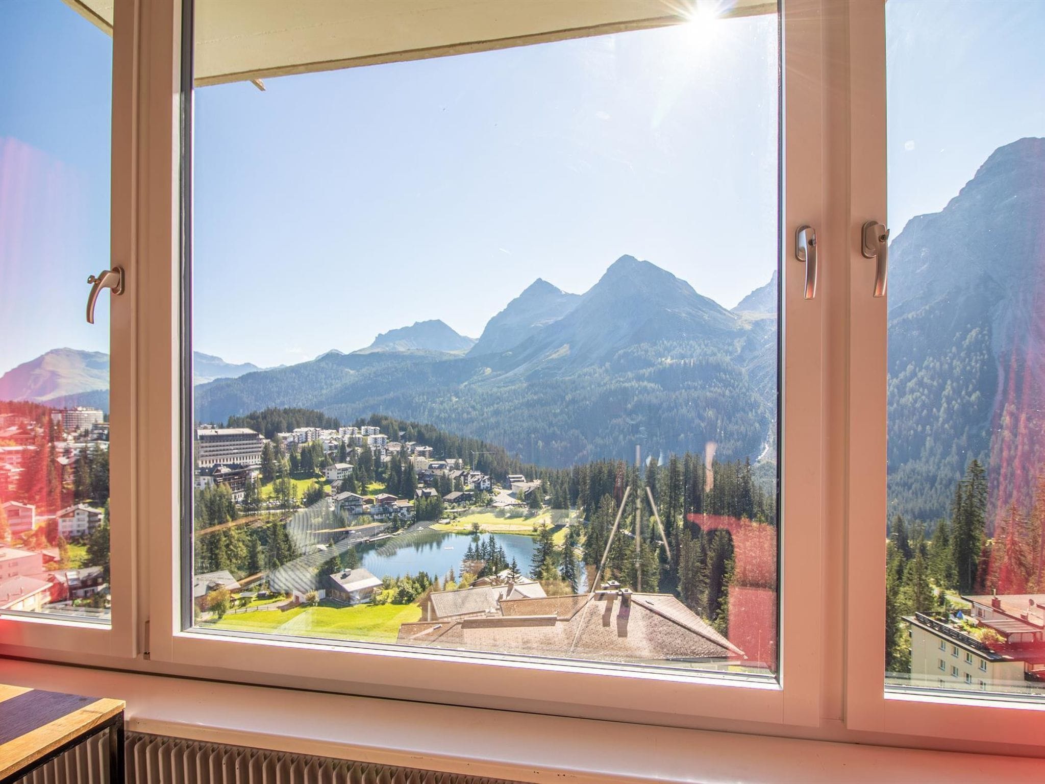 Ein Fenster mit Blick auf eine gebirgige Landschaft, einen See und Gebäude.